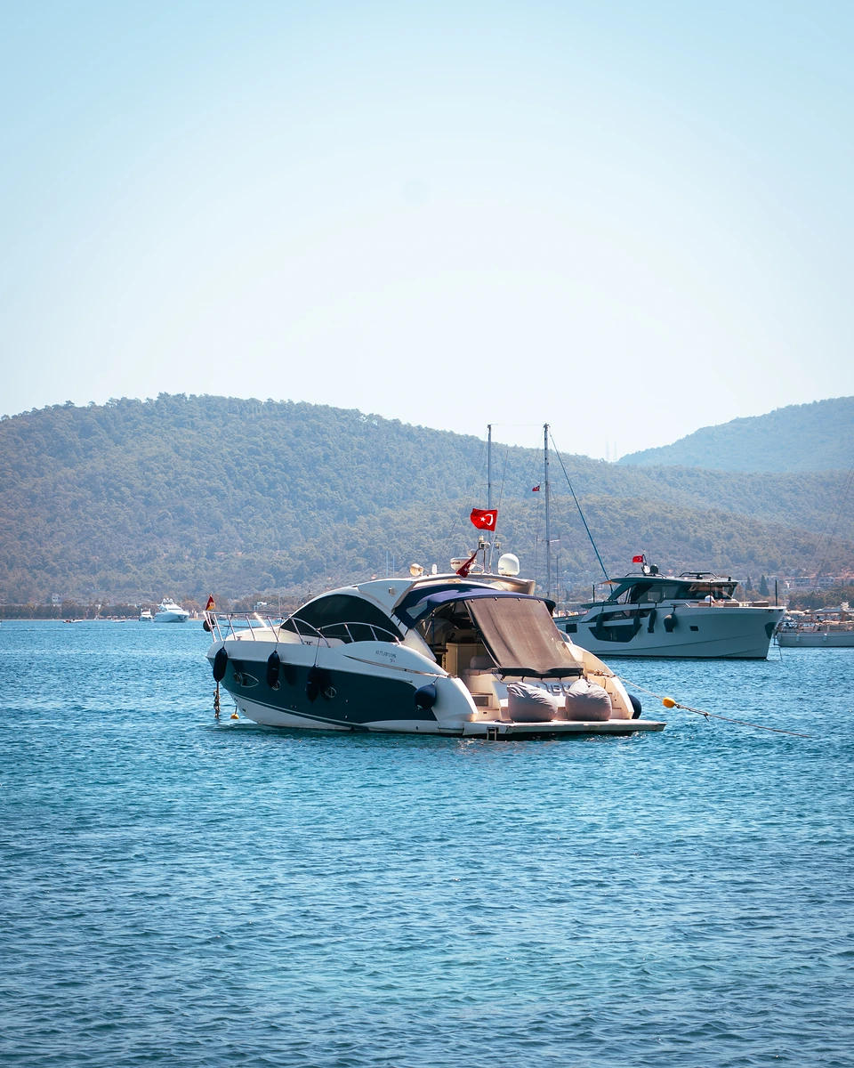 A motor yacht flying a Turkish flag at anchor off Türkbükü, wooded hills beyond