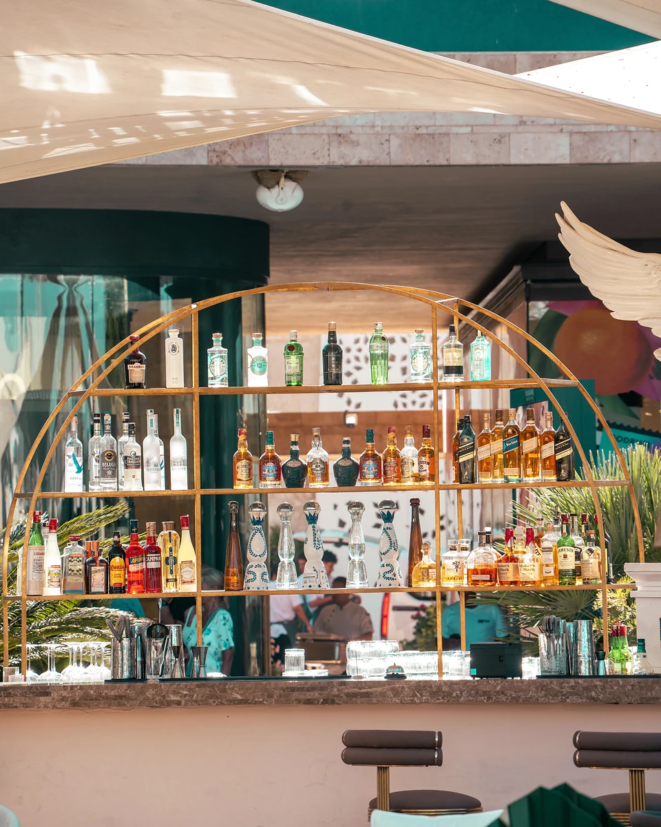 Bottles on an arched brass shelf at a bar in Yalıkavak, a white sculpted wing beside