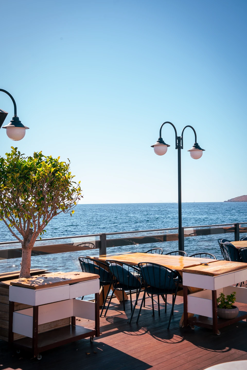 Dark wire chairs at a wooden table on a Yalıkavak seafront deck, twin globe lamps above