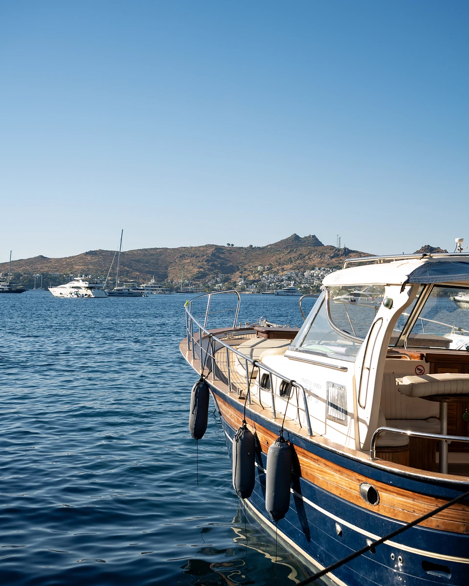 A navy and varnished-wood launch moored in Yalıkavak, yachts and dry hills across the bay