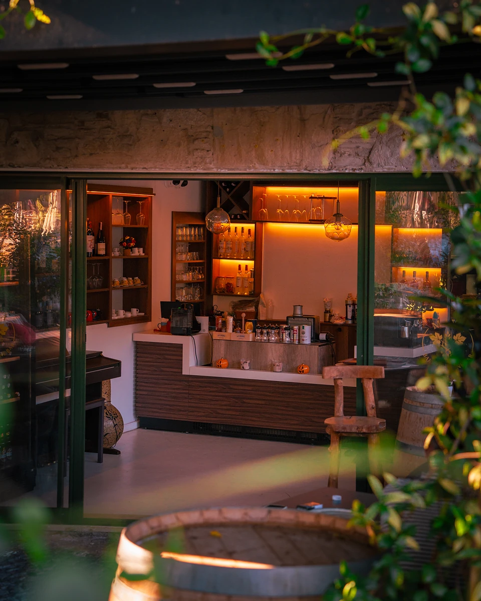 A small bar glowing orange through open glass doors in Yalıkavak, a barrel in front