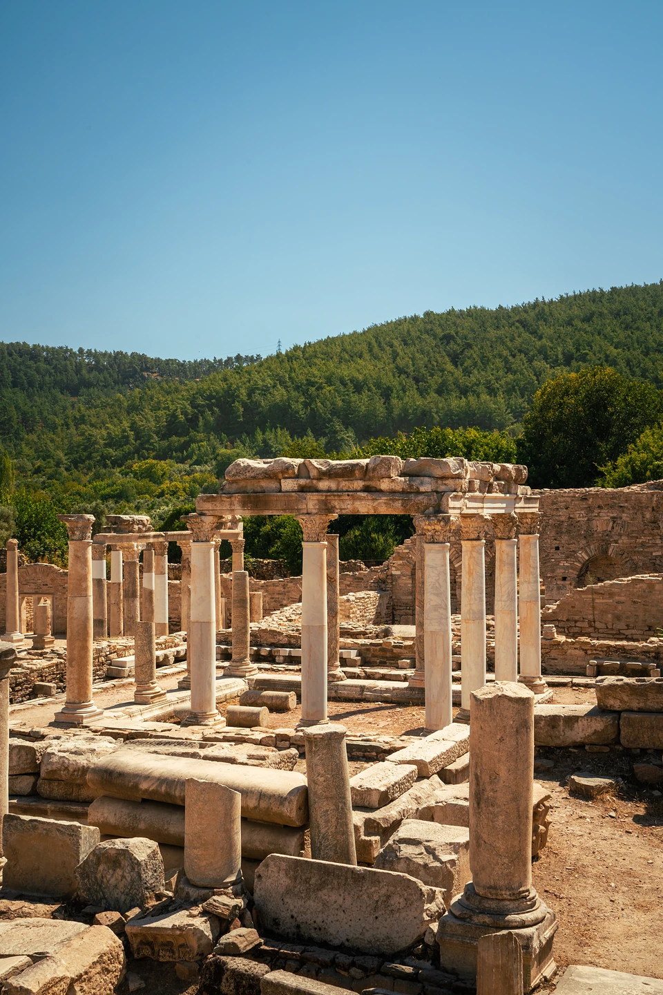 Rows of marble columns at Stratonikeia, one stretch still carrying its stone lintel, forested hills behind