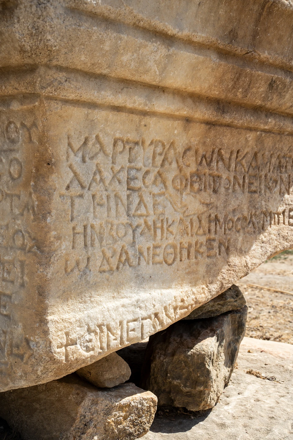 Greek letters and a small cross carved into a marble block resting on rough stones
