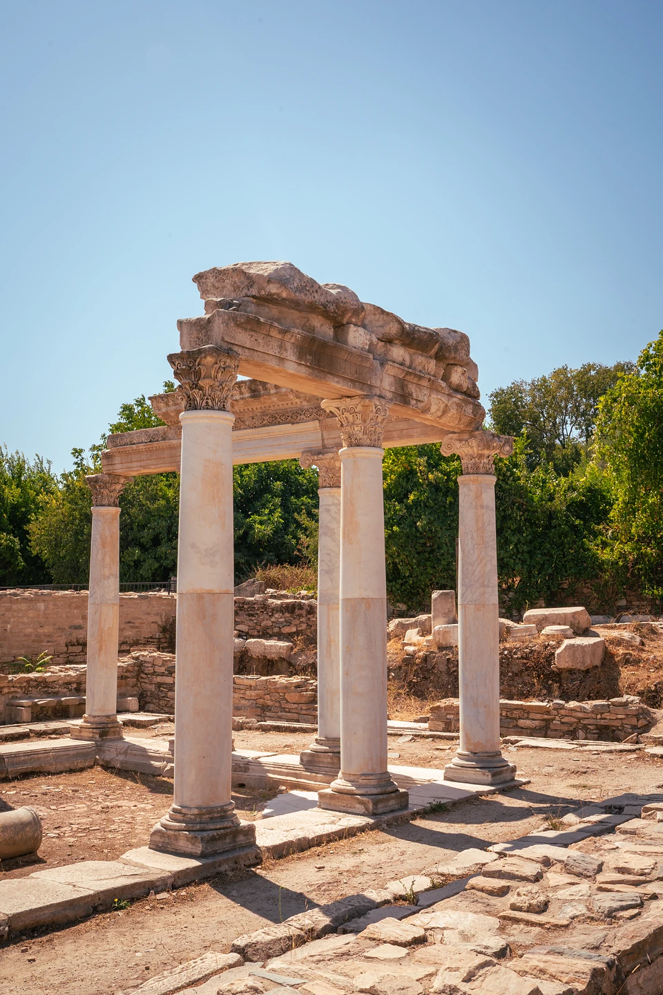 A small colonnade still bearing its stone beams, a paved path running past in the sun