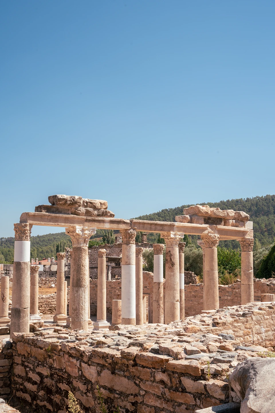 A long colonnade with bright white repairs, rubble walls in front and wooded hills beyond
