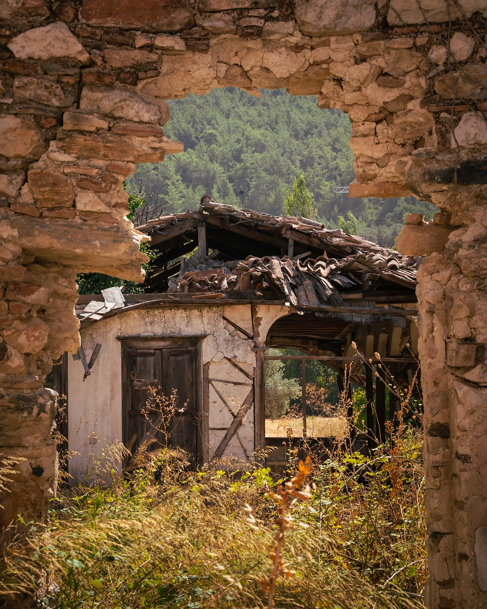 An abandoned house with a collapsing tiled roof, framed by a gap in a ruined wall