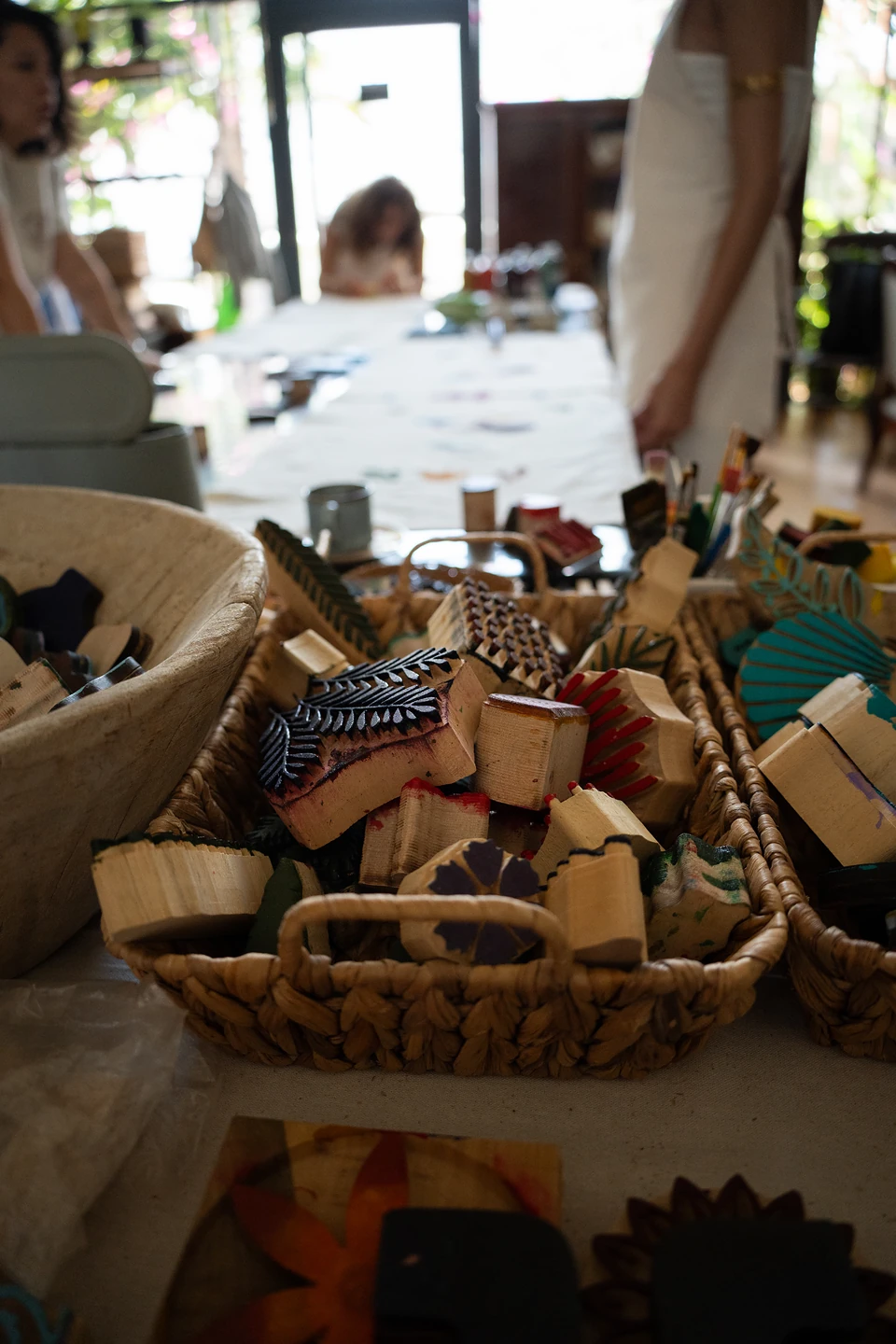 Wicker baskets heaped with carved wooden printing blocks, the long worktable blurred behind