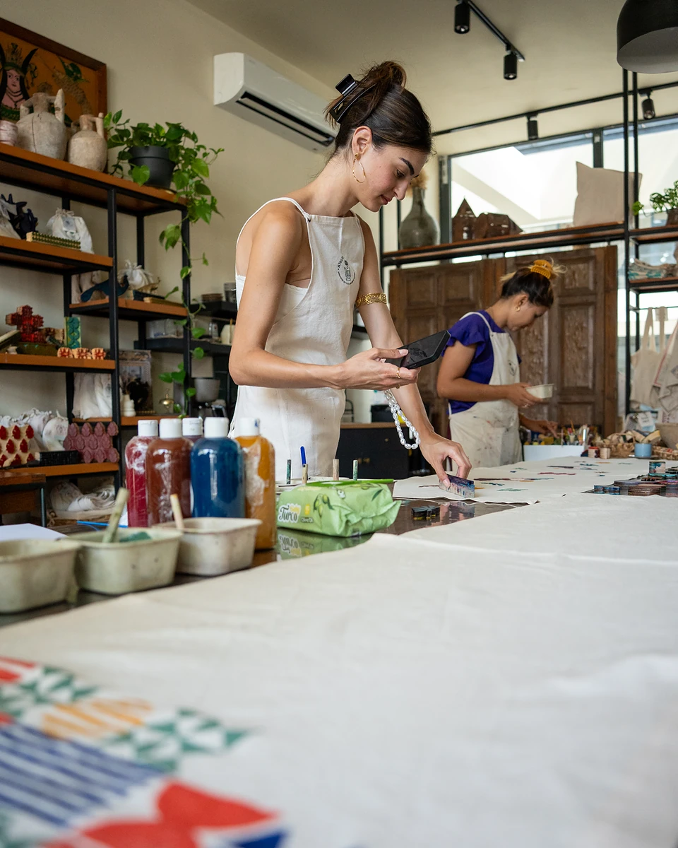 One of us pressing a small block onto cloth, another woman working at the far end