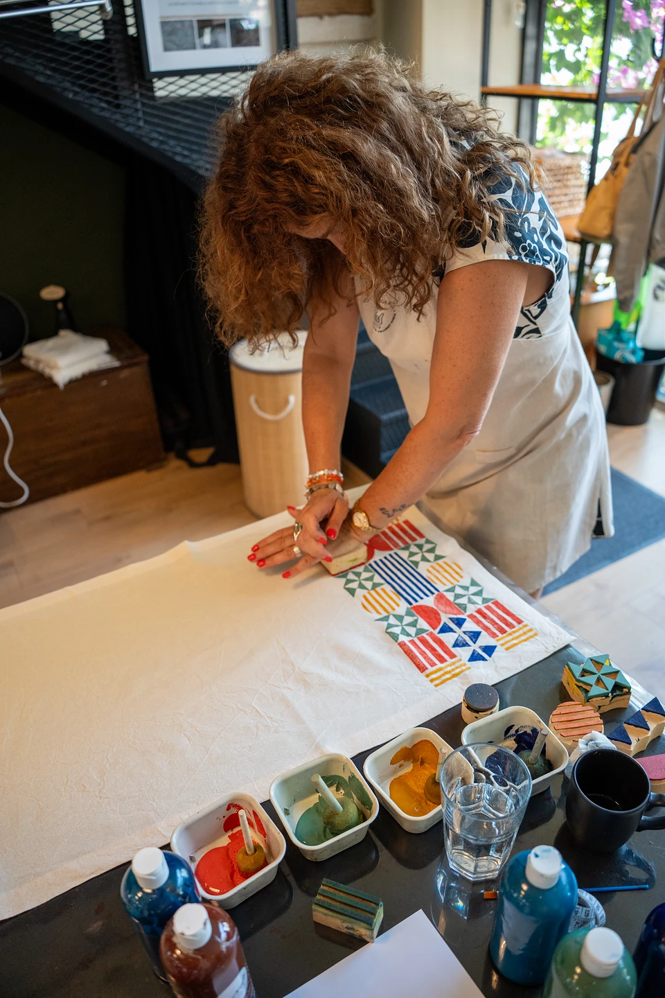 A woman bent over the table, stamping a geometric grid of stripes and pinwheels onto cloth