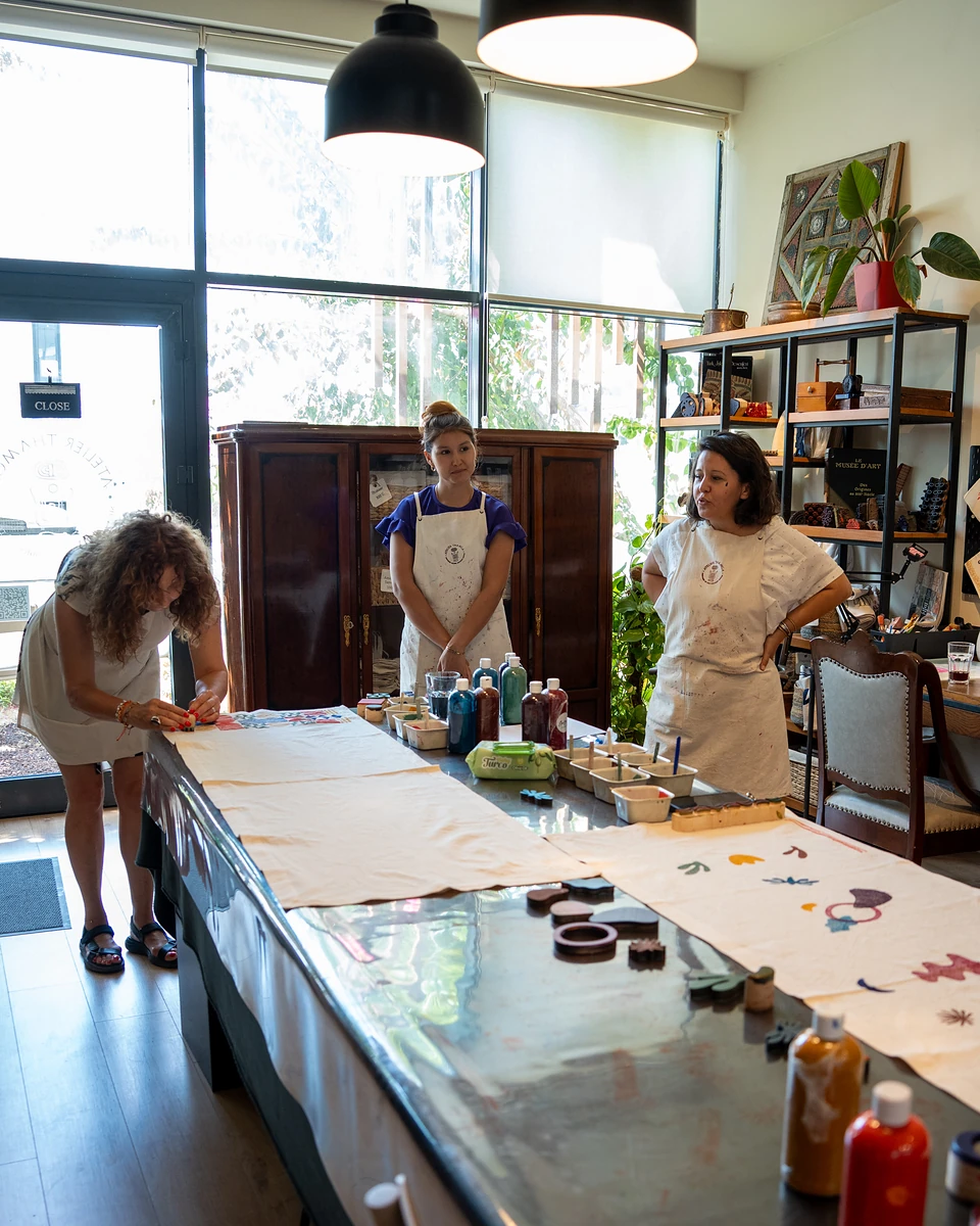 A woman printing at the table's end while two others in aprons look on