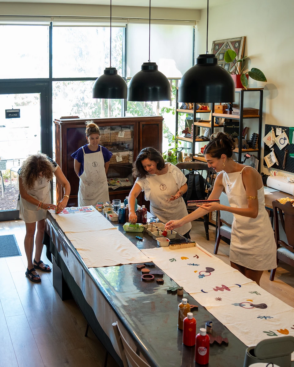 Four women at work along the table under three black pendant lamps, big windows behind