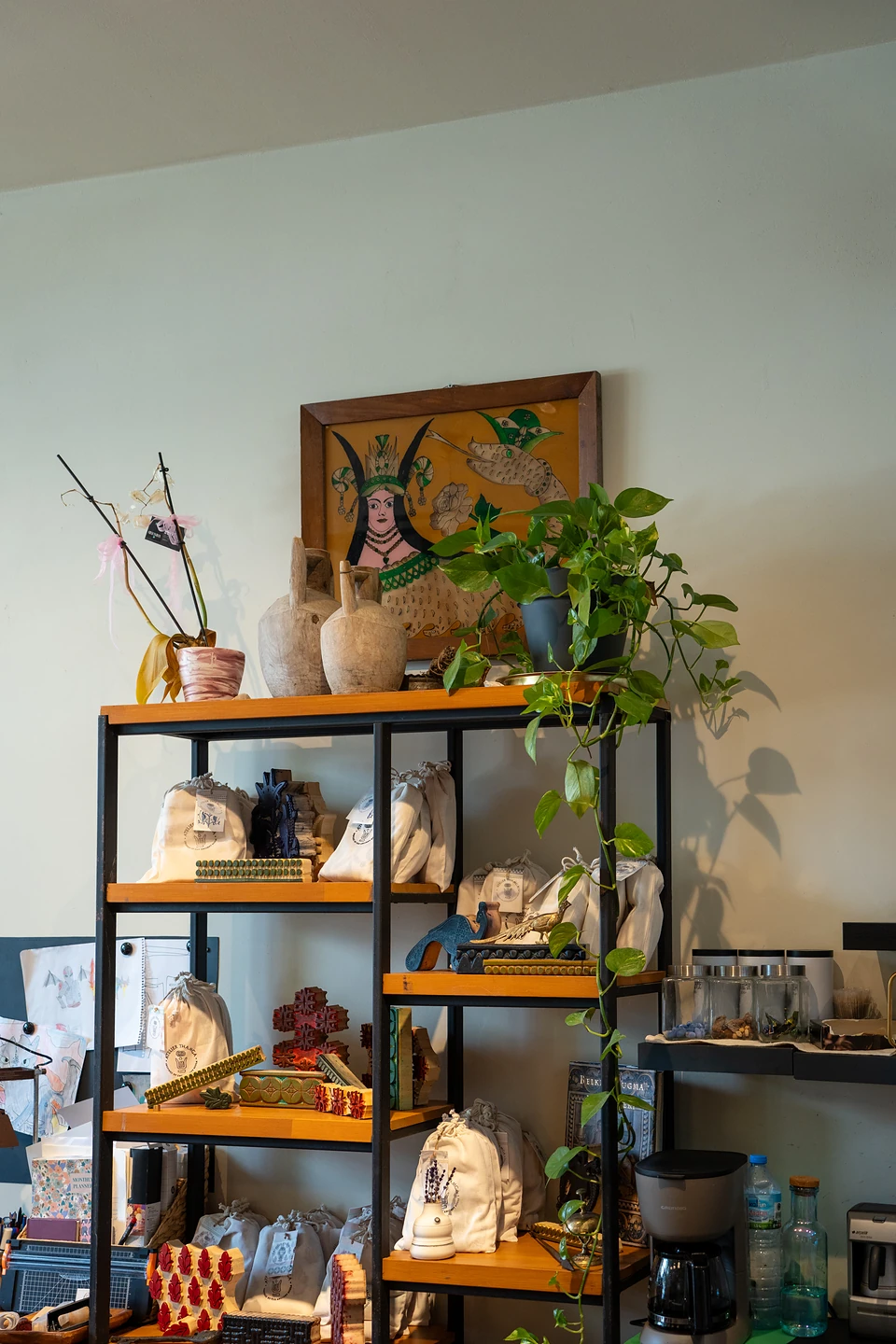 Shelves of cloth bags, printing blocks and clay jugs under a painting of a crowned woman