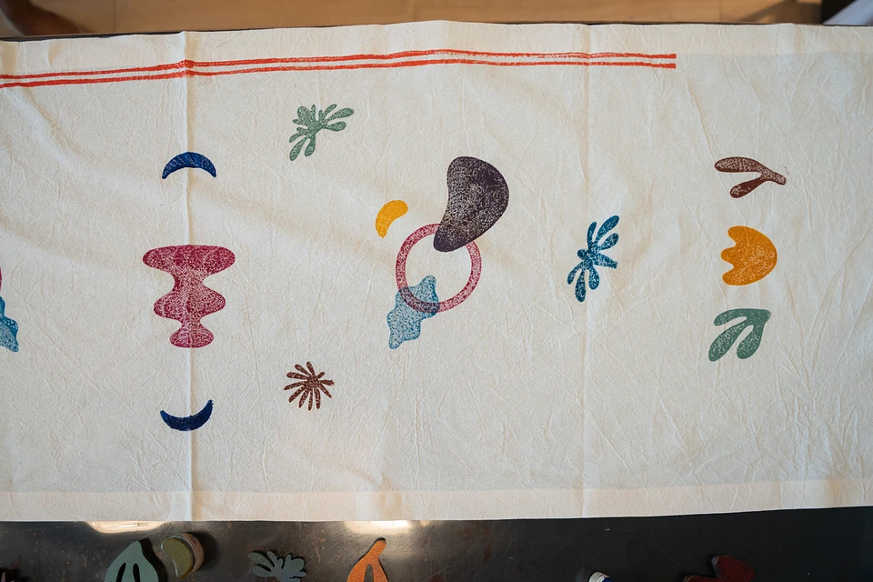 Printed shapes scattered loosely along a cream cloth: crescents, a ring, a bean, leaves and sprigs