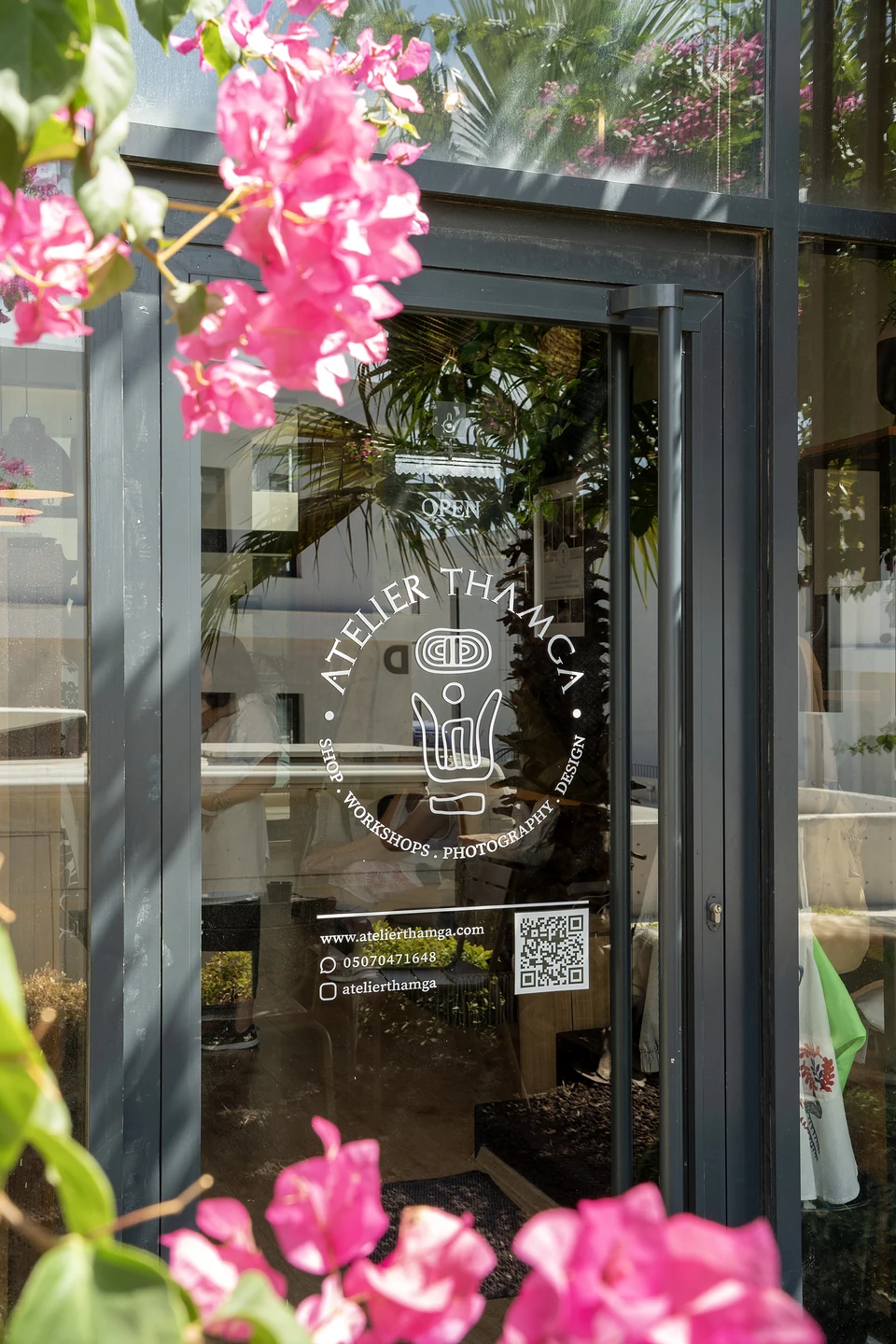 Pink bougainvillea framing the glass door of Atelier Thamga, its name in a white circle