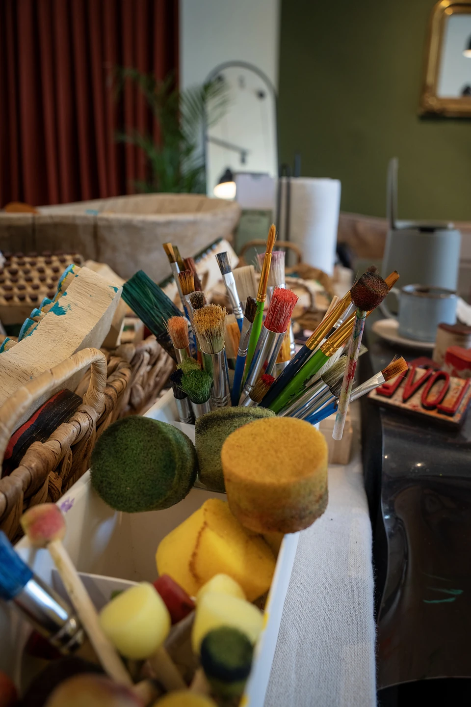 A cluster of paintbrushes and round sponge daubers on the worktable, a gilt mirror beyond