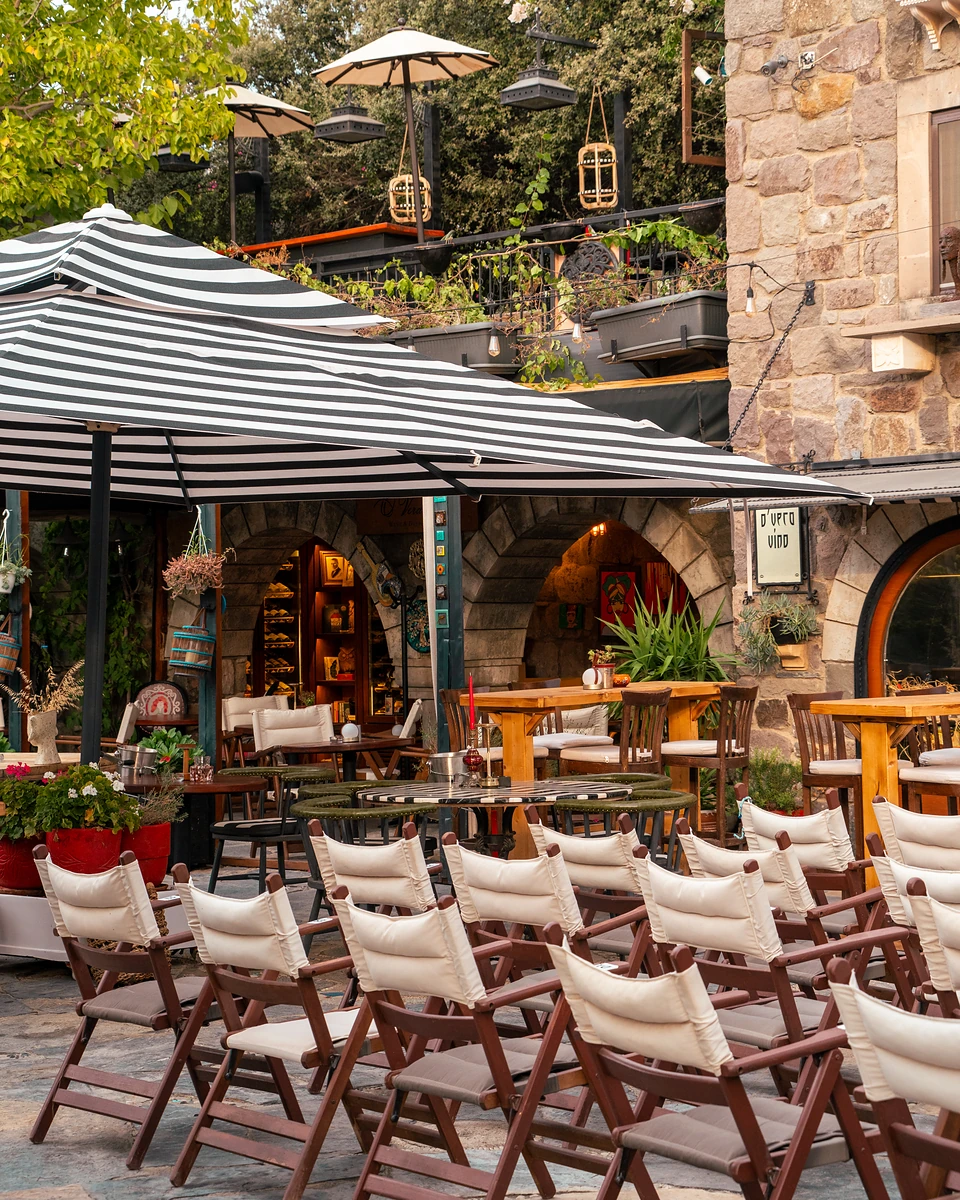 Rows of canvas folding chairs under striped umbrellas before the stone arches of Dibeklihan