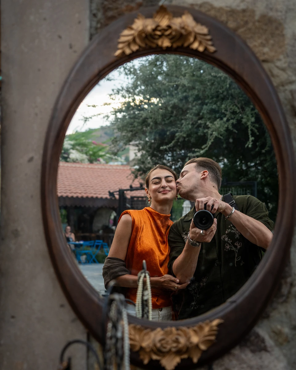 The two of us reflected in an oval mirror with gilt flowers, camera in hand