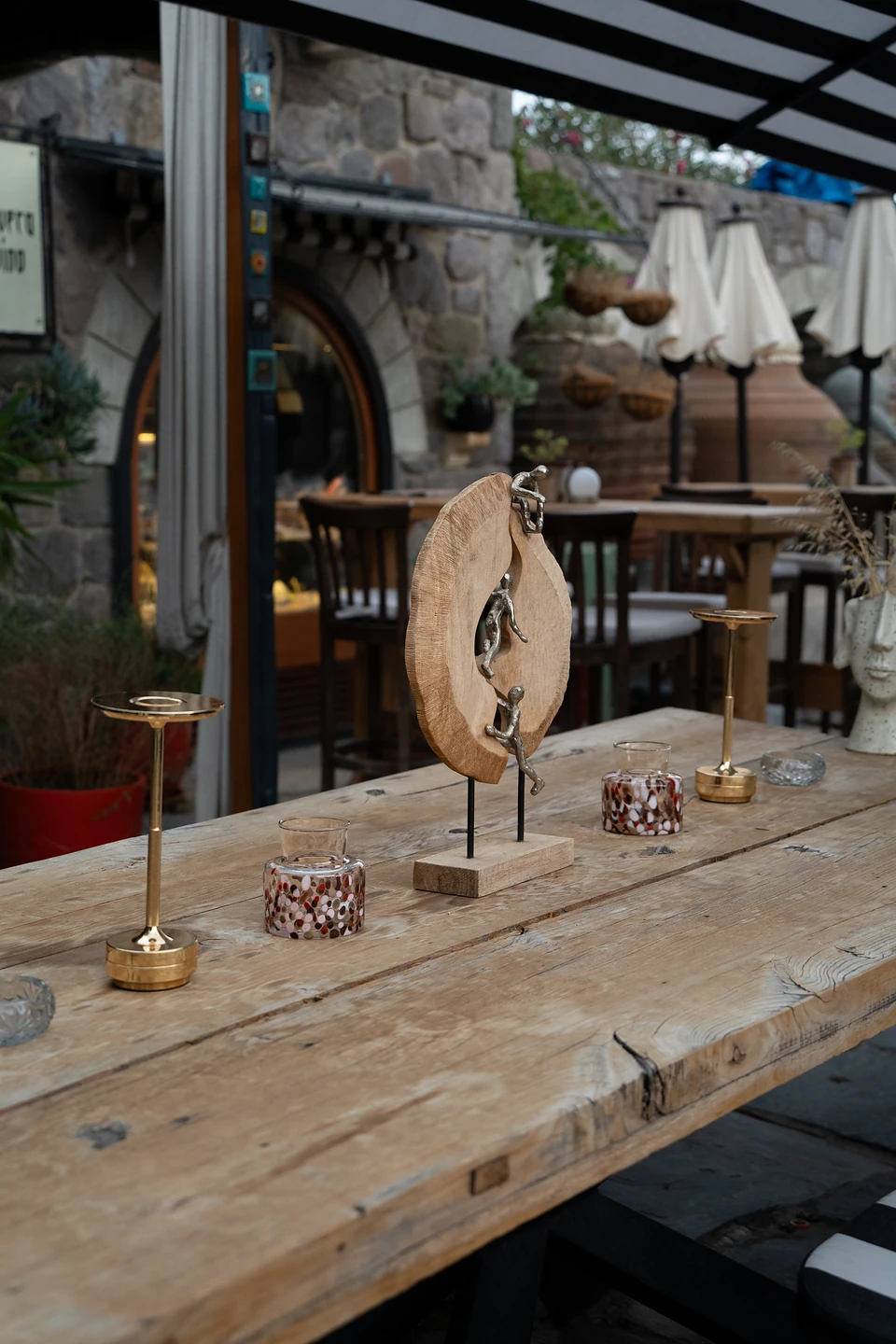 Small metal figures climbing a wooden ring, a sculpture on a weathered table between gold lamps