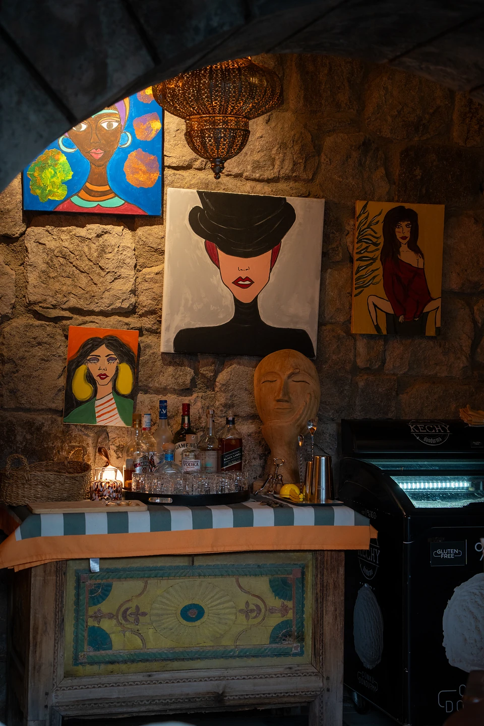 Painted portraits of women on a stone wall above a bar and a sculpted head