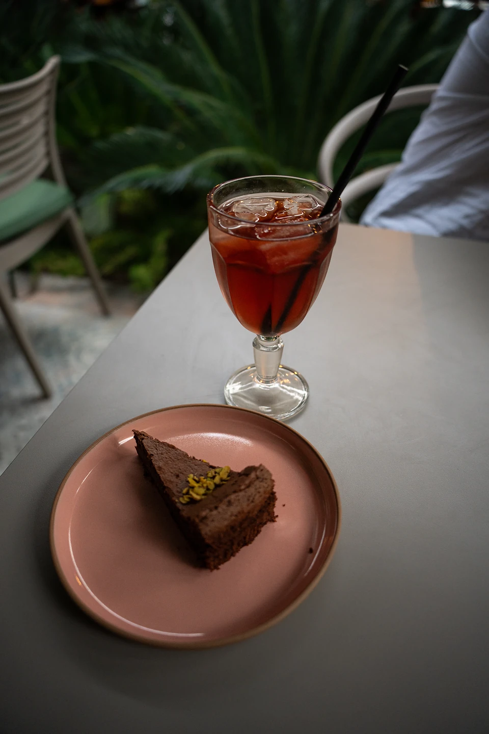Chocolate cake sprinkled with pistachio on a pink plate, an iced red drink beside it