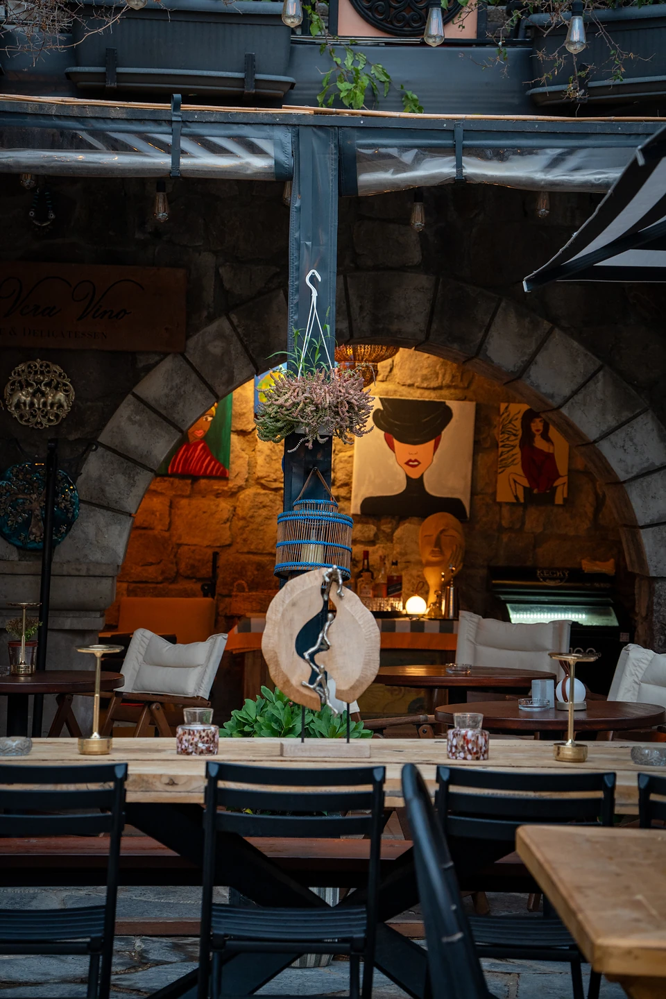 Long tables and black chairs before a lamplit stone arch hung with painted portraits