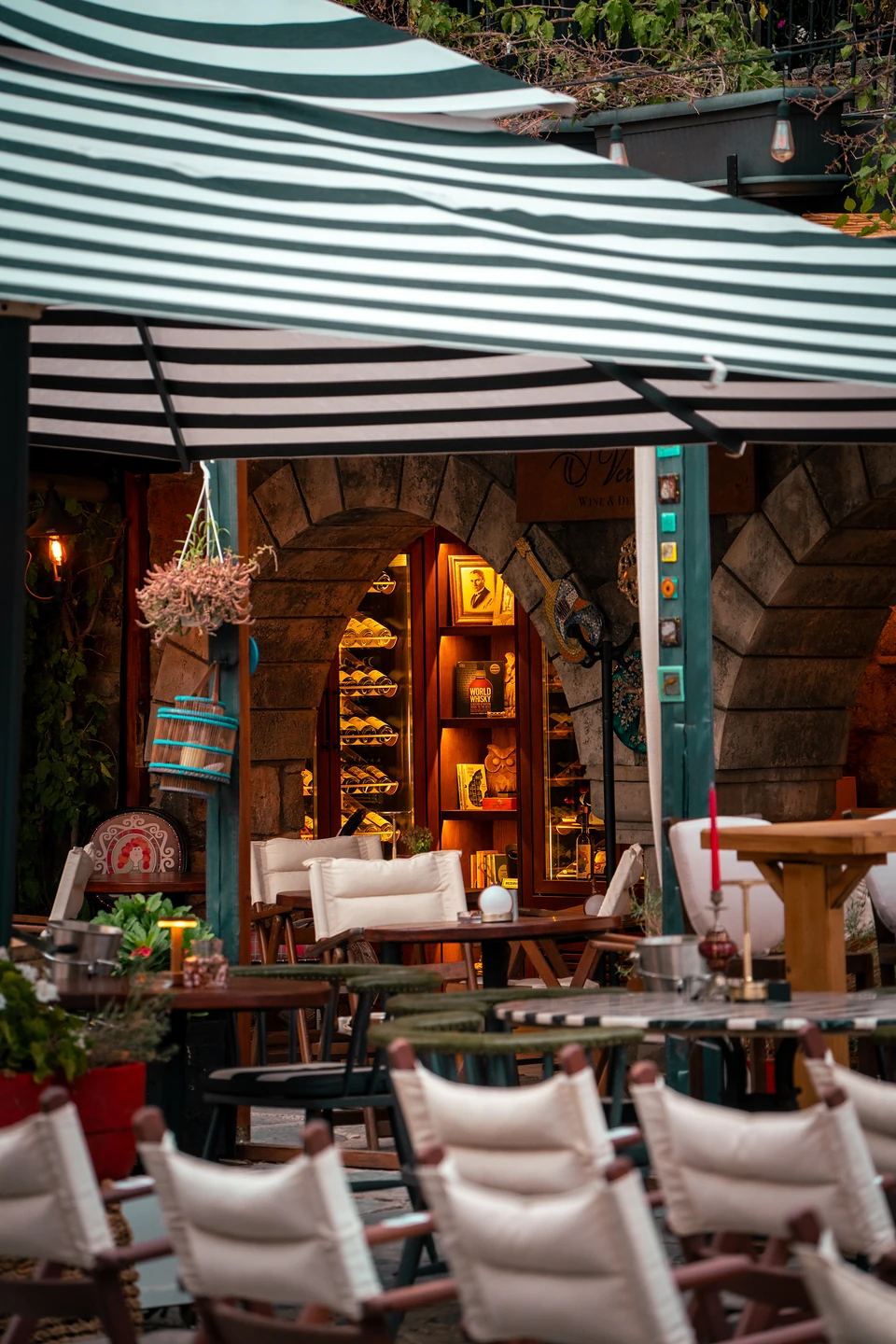 Under a striped awning, a stone arch opening onto glowing shelves of wine bottles