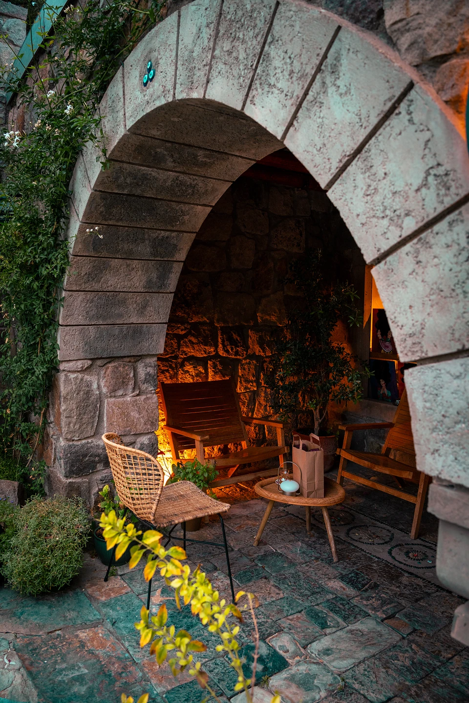 A glowing stone archway sheltering wooden lounge chairs and a rattan seat around a low table