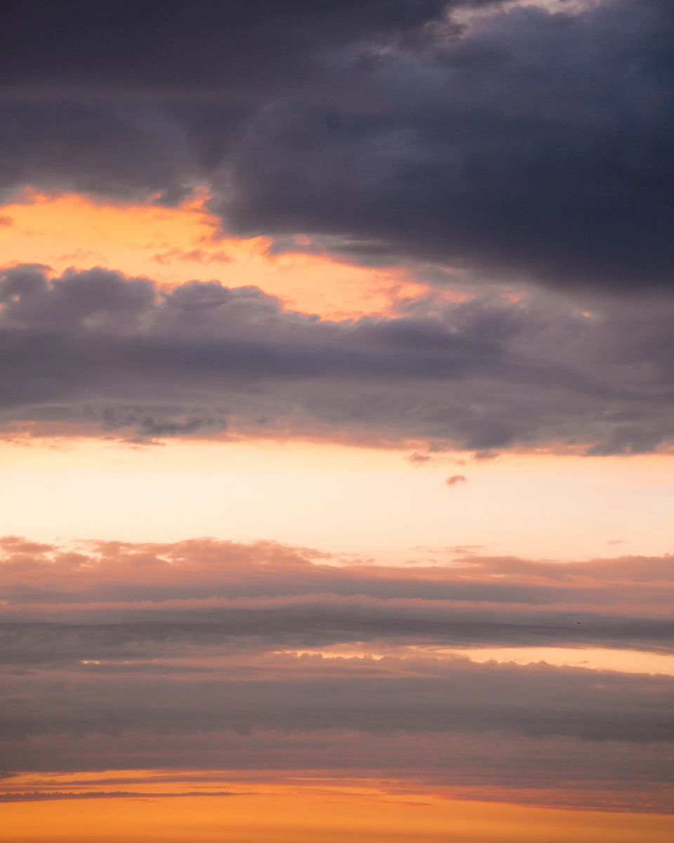 Layers of dark grey cloud with bands of orange sunset glowing between them