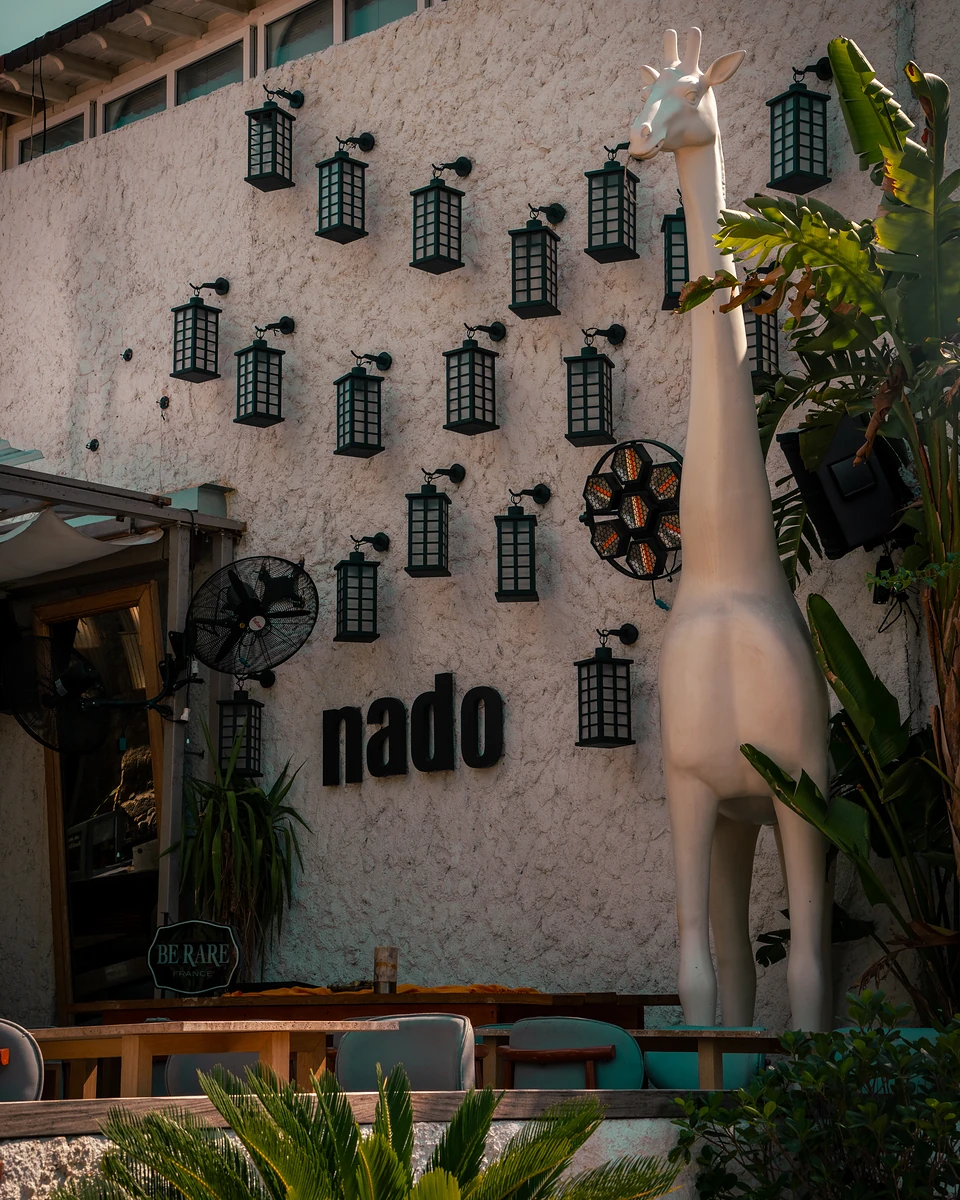 A white giraffe sculpture by a wall of black lanterns and the word ‘nado’ in Bodrum