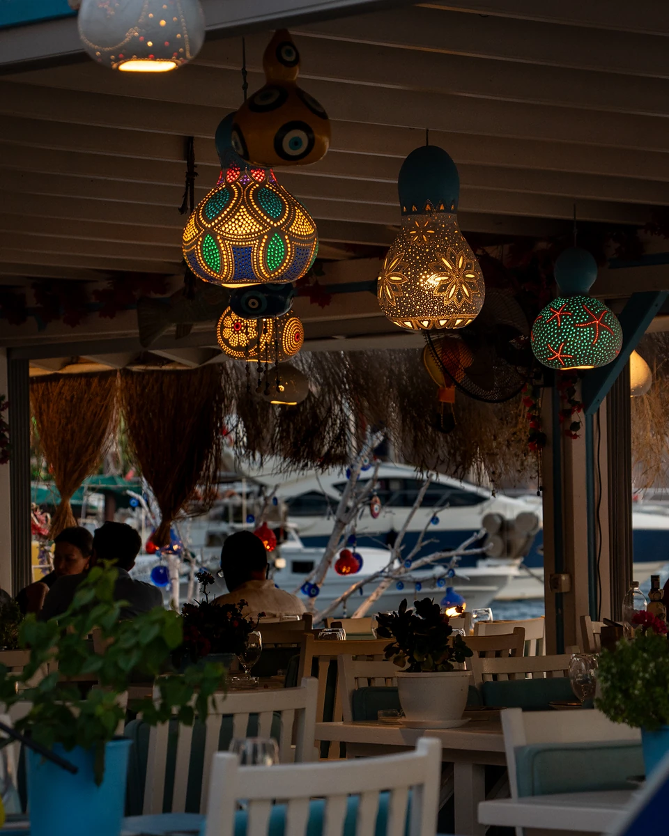 Pierced and painted gourd lamps glowing above diners at a waterside restaurant in Gümüşlük