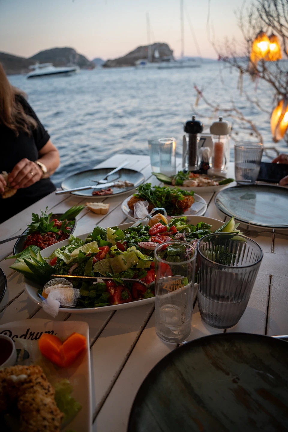A large green salad, a red dip and small plates shared by the water in Gümüşlük