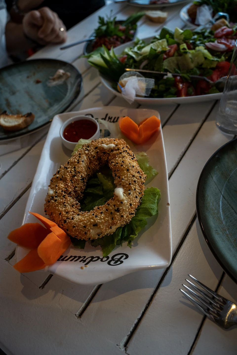 A sesame-crusted ring with a red dip and carrot petals on a plate printed ‘Bodrum’
