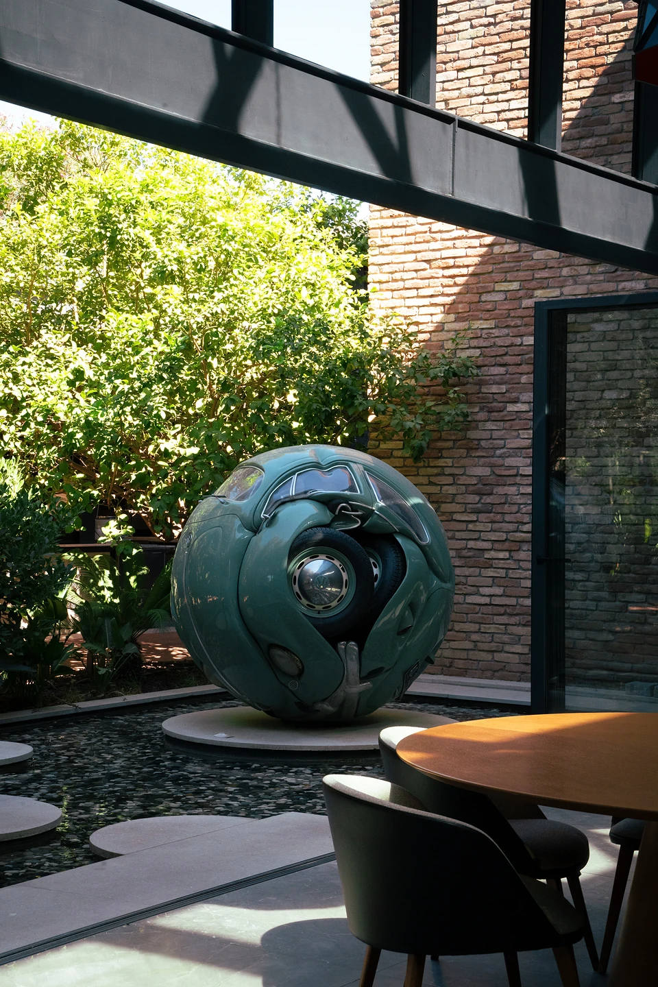 The green car sphere showing a wheel and hubcap, seen past a round wooden table
