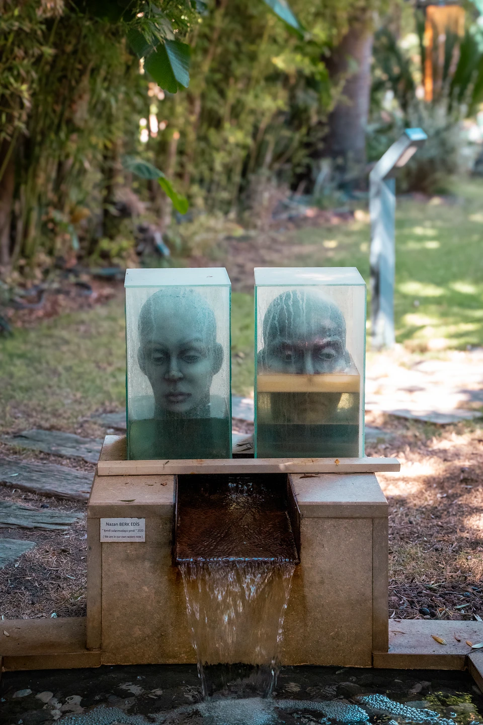 Two sculpted heads in glass cases above a small fountain, water spilling into a pool