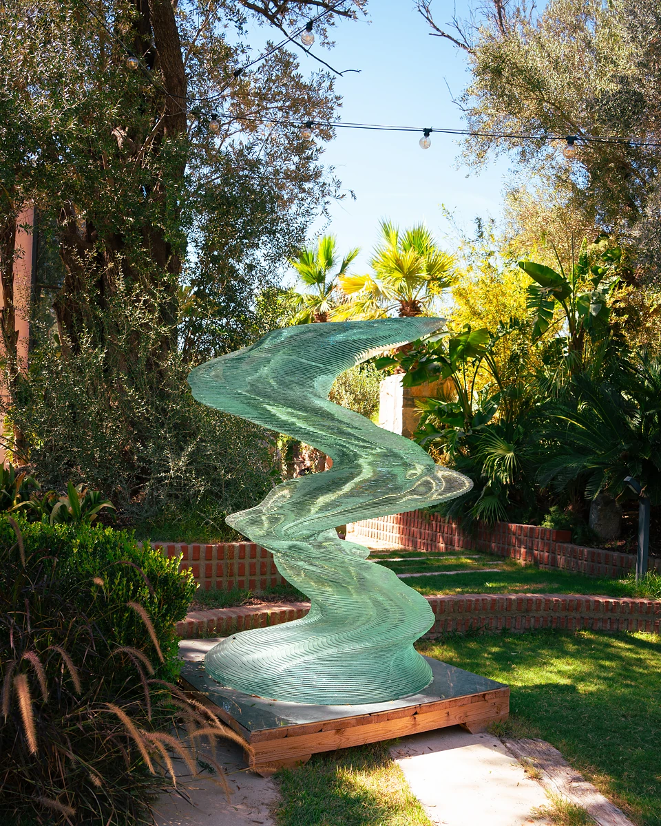 A twisting sculpture of stacked green glass on a lawn at Zai, string lights overhead