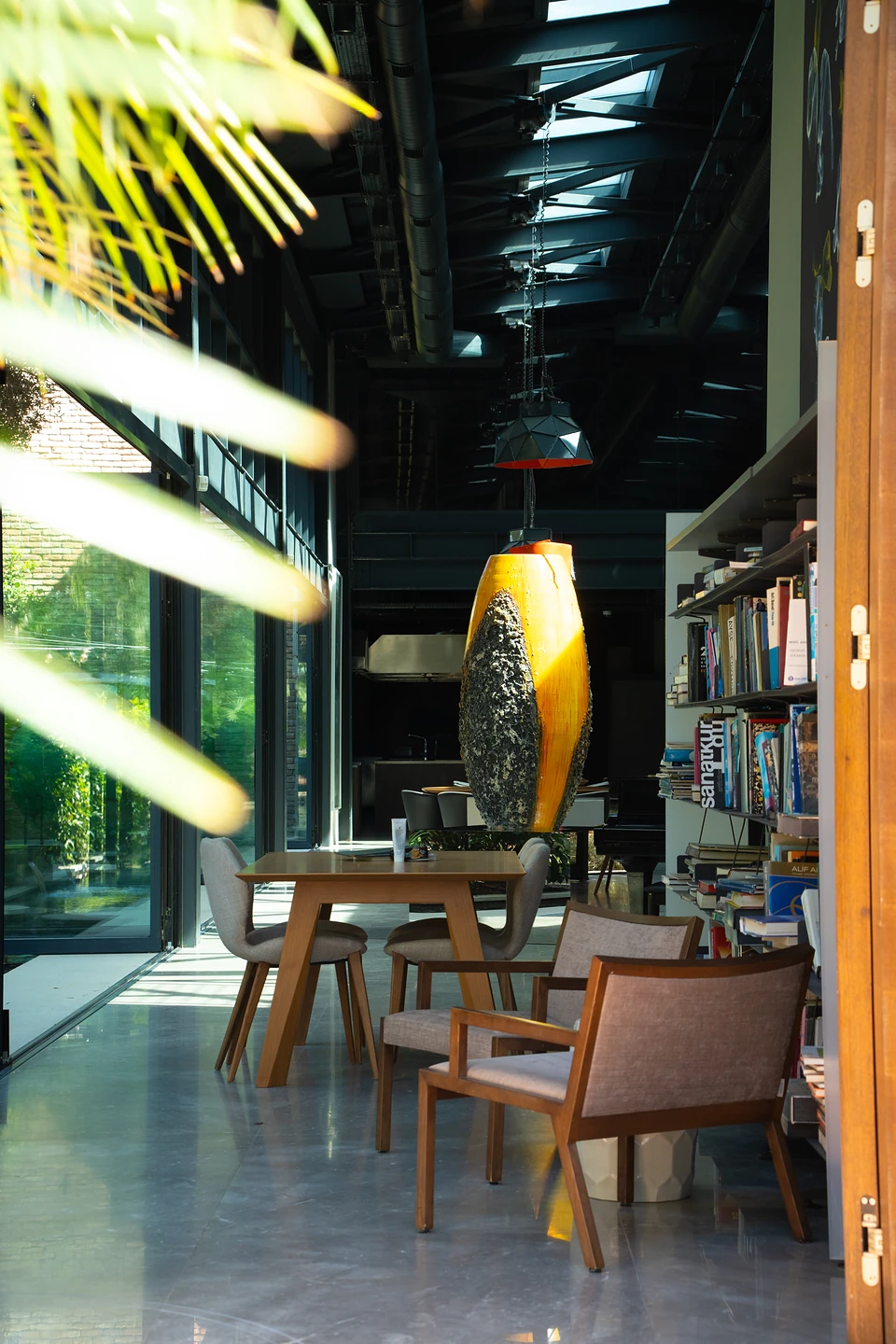 Bookshelves, armchairs and a wooden table in the glass hall, a tall orange sculpture beyond