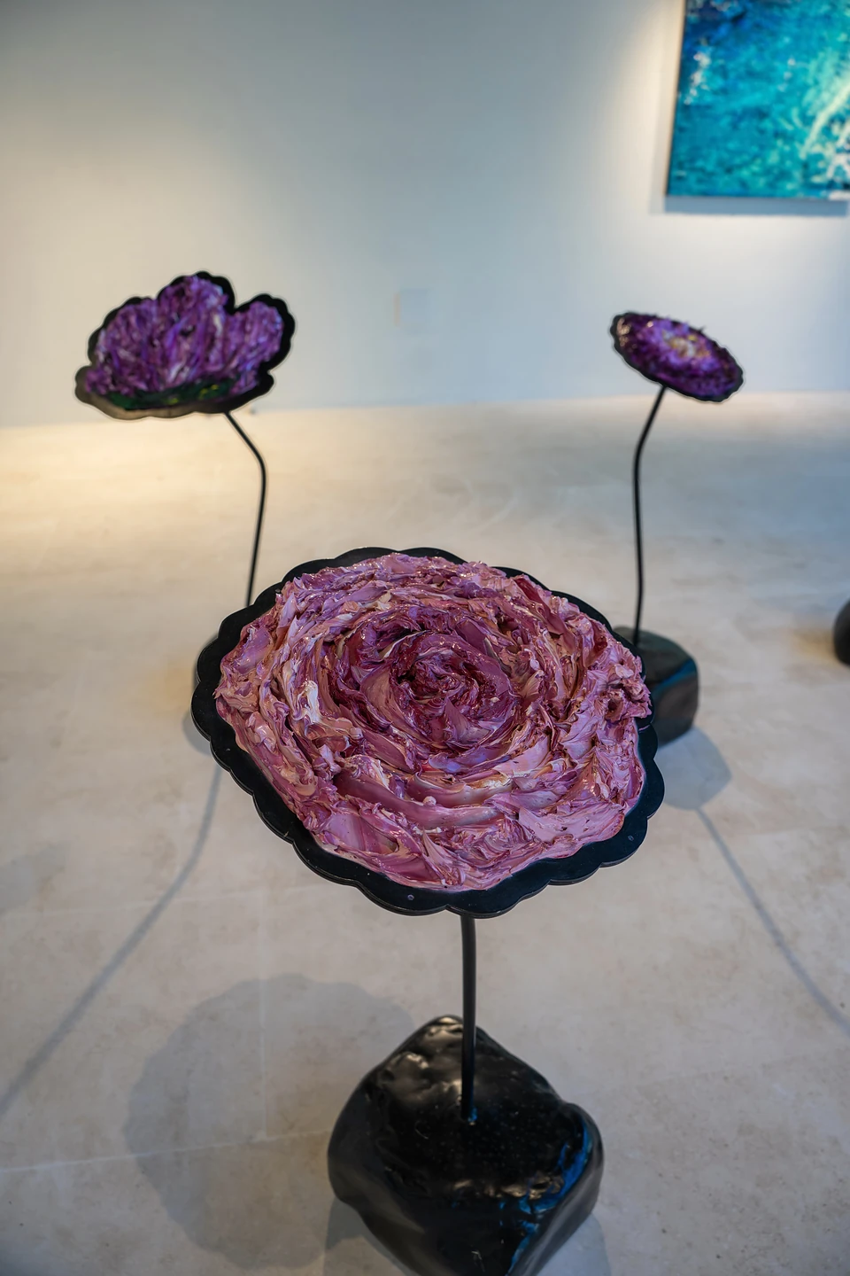 Sculpted flowers with thick, swirled purple and pink petals on black stems in a white gallery