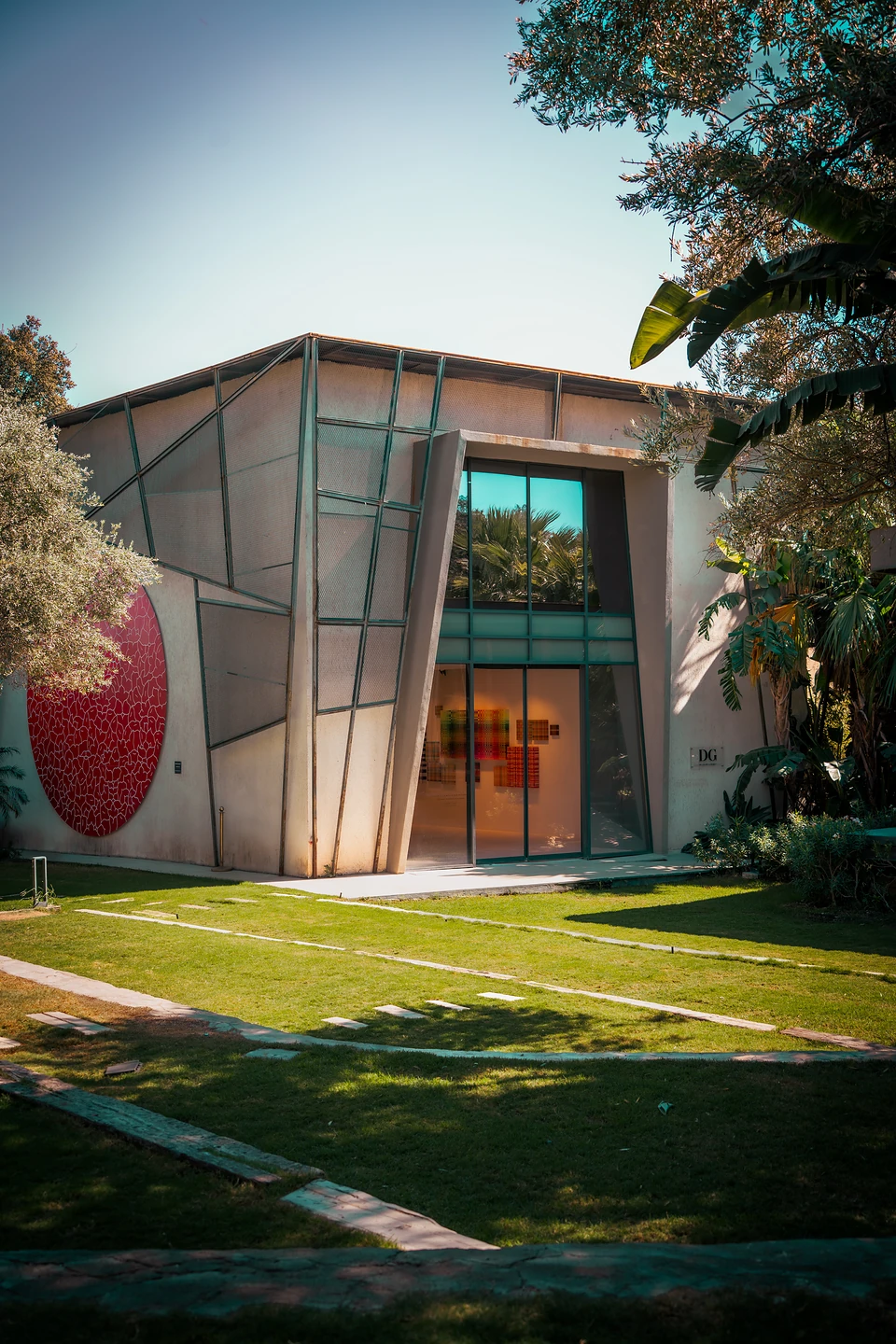 An angular gallery at Zai, a large red disc on its facade, seen across the lawn