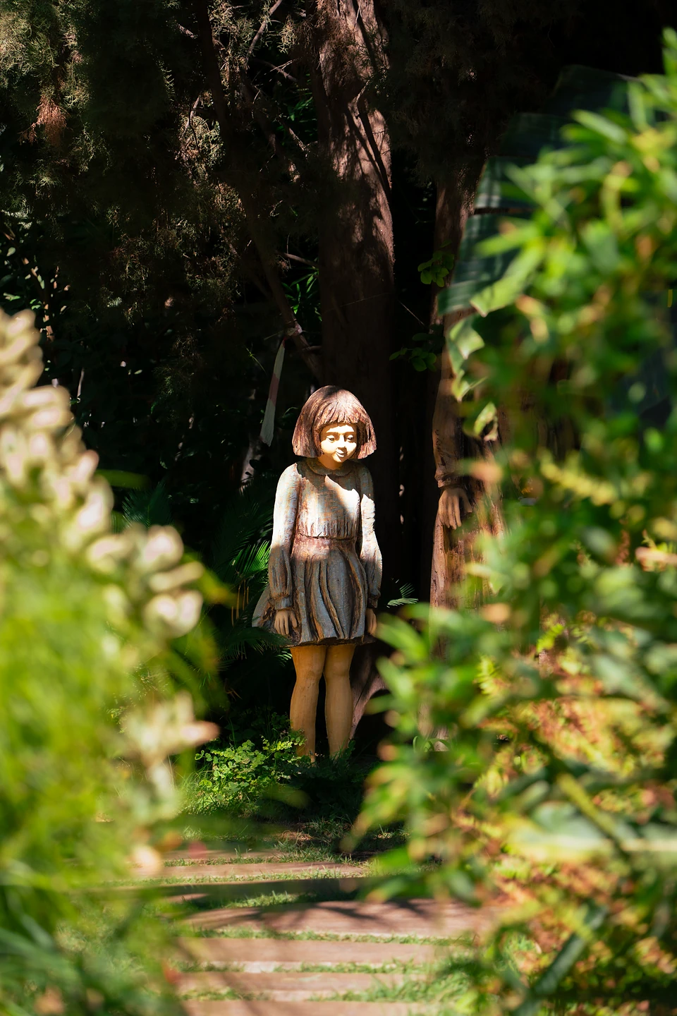 A wooden statue of a girl at the end of a shady path, framed by leaves
