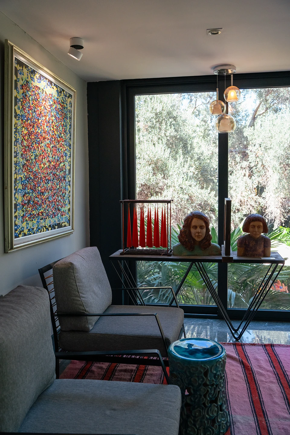 Two painted busts on a console by a window, beside grey armchairs and a speckled painting