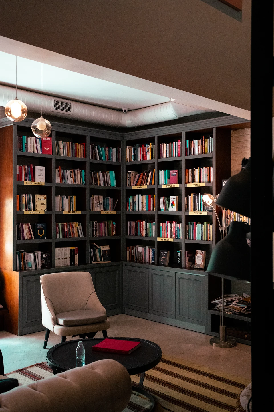 Grey corner shelves of books labelled by subject, a cream armchair and a low black table
