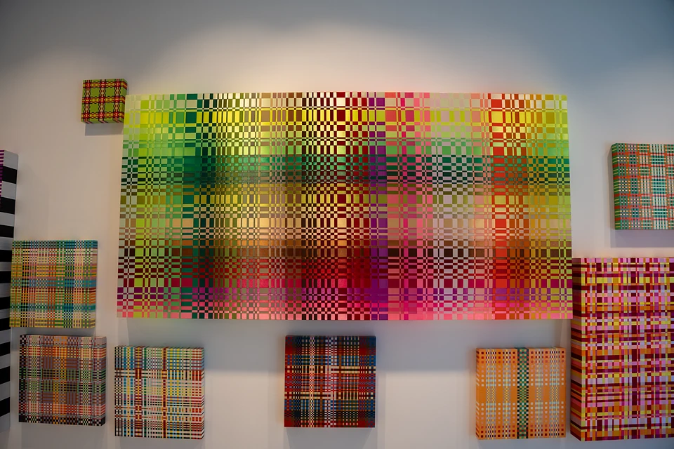 Small plaid canvases around a large one shading from yellow and green to pink