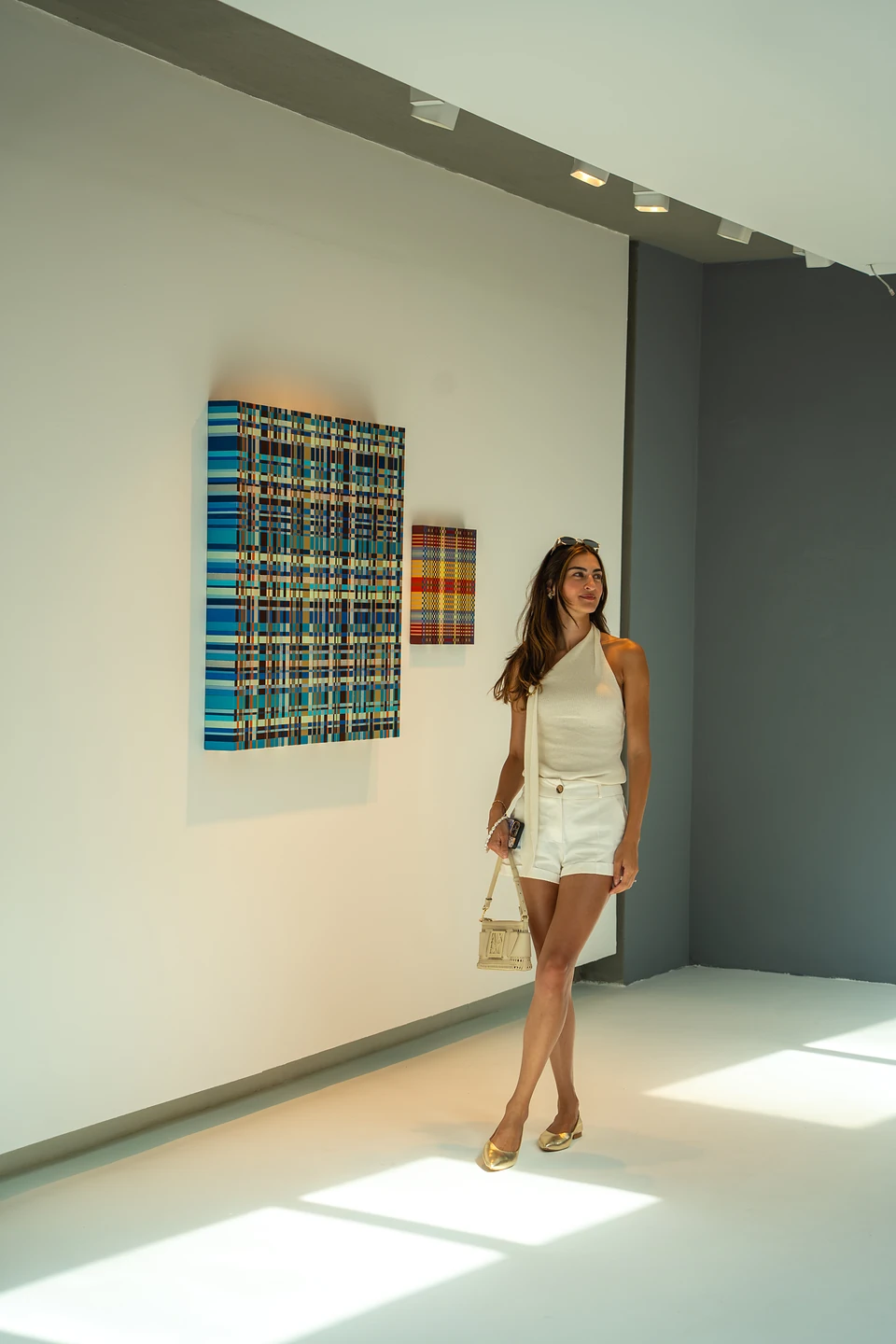 One of us walking past a large blue plaid painting in a sunlit white gallery