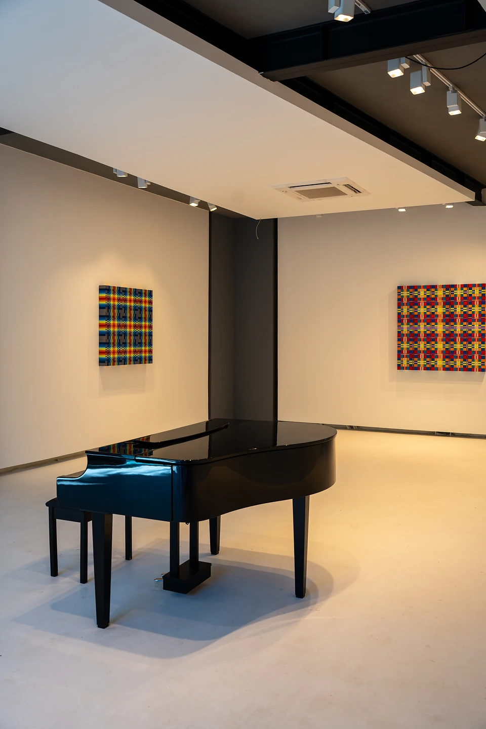A lone grand piano in a white gallery, with two bright plaid paintings on the walls