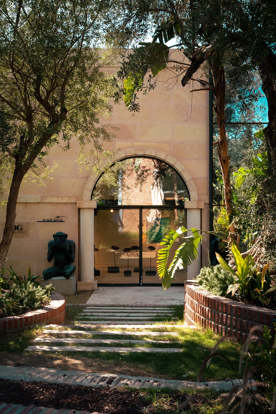 A stone path to an arched glass doorway at Zai, a dark seated sculpture beside it