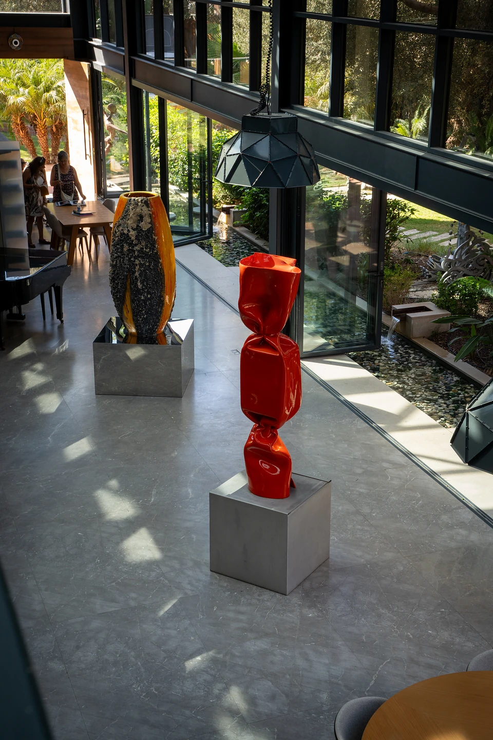 Seen from above, a red wrapped-sweet sculpture and a tall orange one on steel plinths