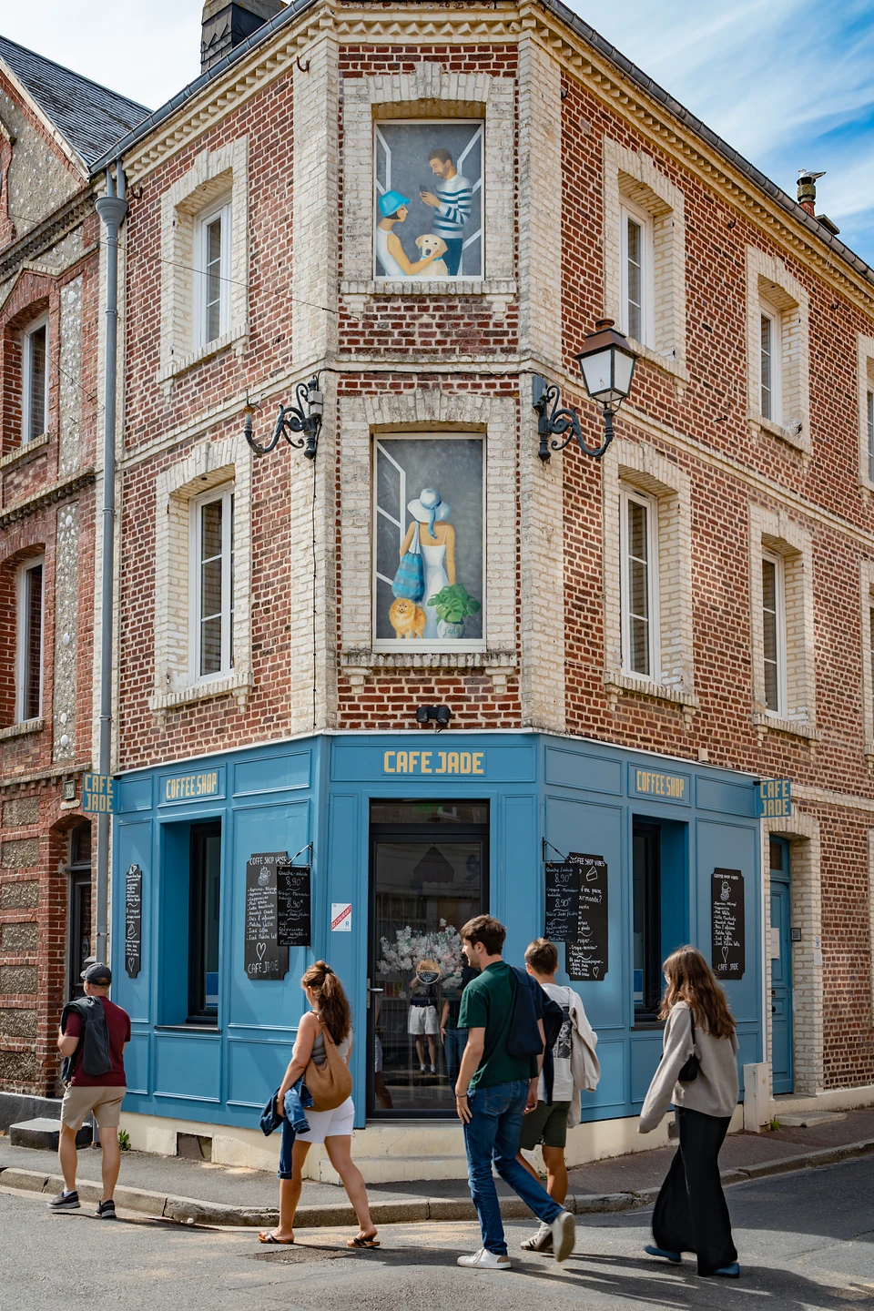The blue corner shopfront of Cafe Jade, painted figures in its upper windows, people walking past
