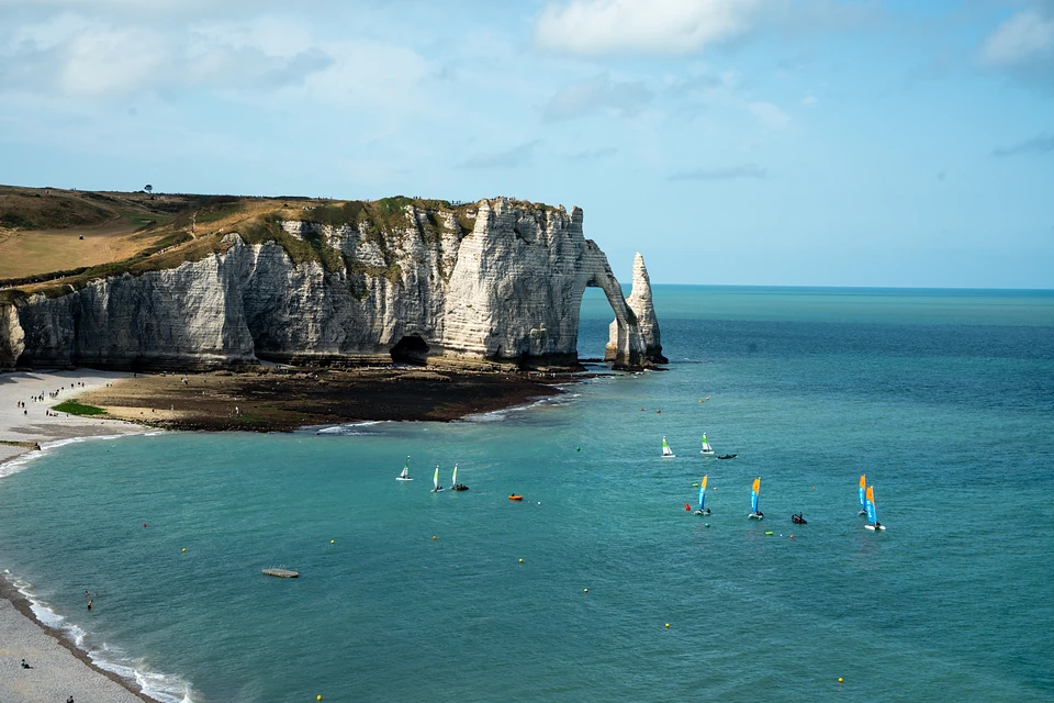 Small sailboats with bright sails in the bay below the chalk arch and the Needle
