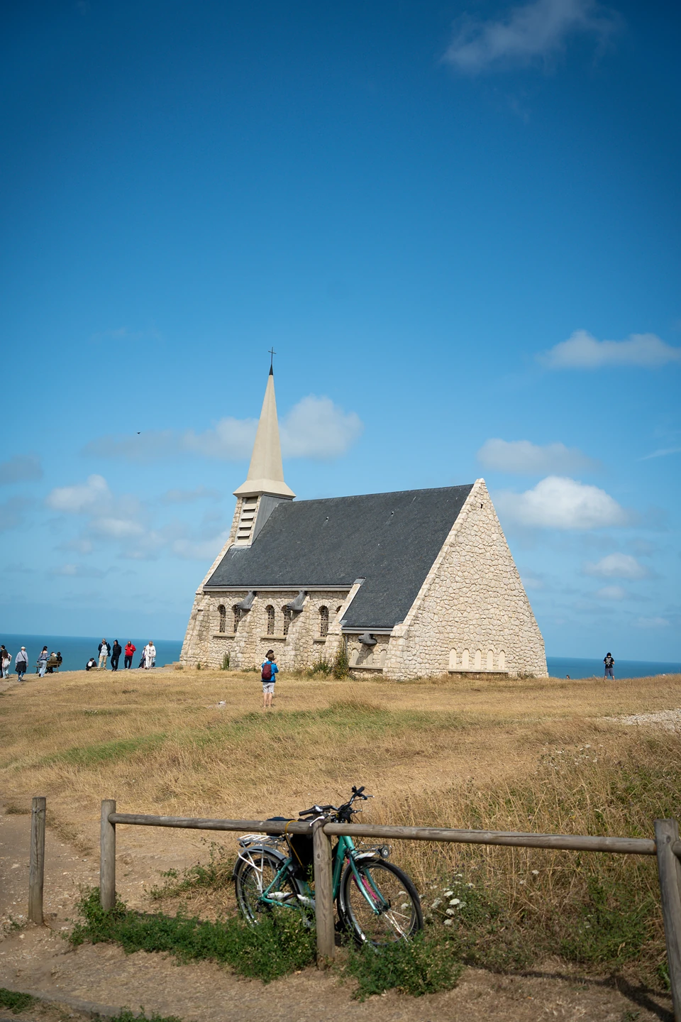 A stone chapel with a slender spire on the clifftop, a bicycle leaning on a fence
