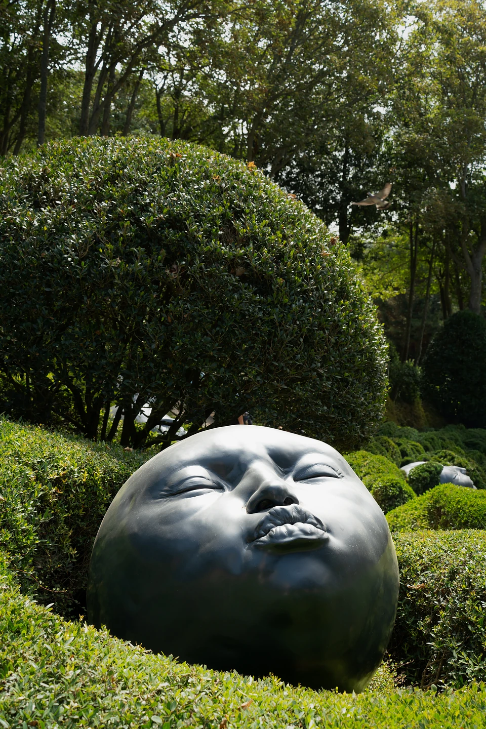 A giant sculpted face with closed eyes and pursed lips among hedges at Les Jardins d'Étretat
